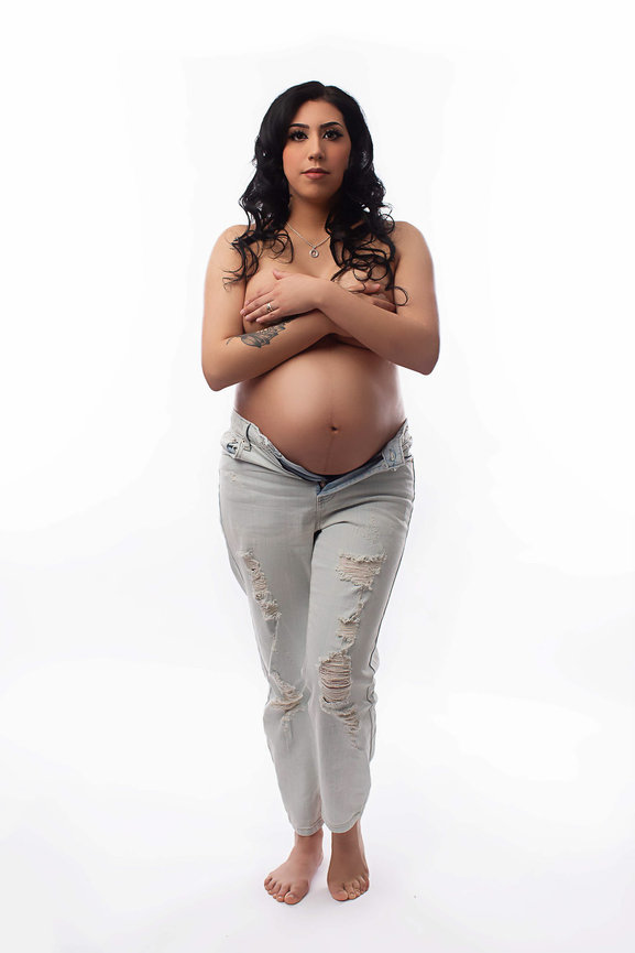 Pregnant woman standing with legs crossed wear jeans and topless arms crossed covering her breasts bare pregnant belly photo taken during maternity photoshoot by maternity photographer Dreamworks Photography in Kansas City