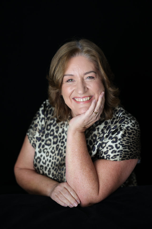 Smiling woman in a leopard print top posing against a black background. Business content photos melb