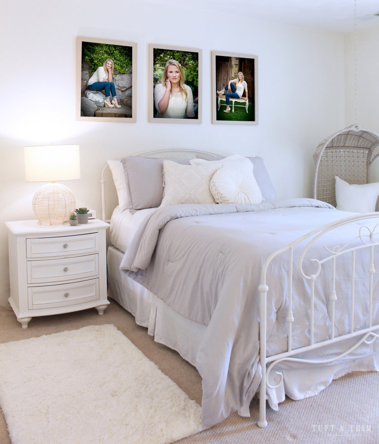 A bedroom in white with 3 beautiful portraits hanging on the wall.