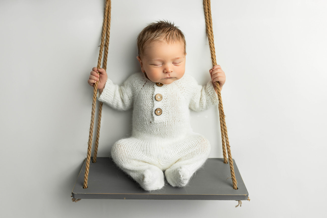 Newborn baby posed sitting up on swing against neutral background