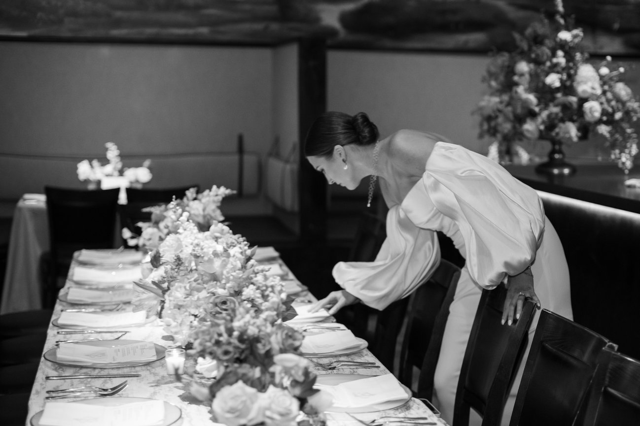 Bride in white dress leaning over florals at Rehearsal Dinner table in Birmingham Alabama. Alabama wedding photography by Heather Durham.