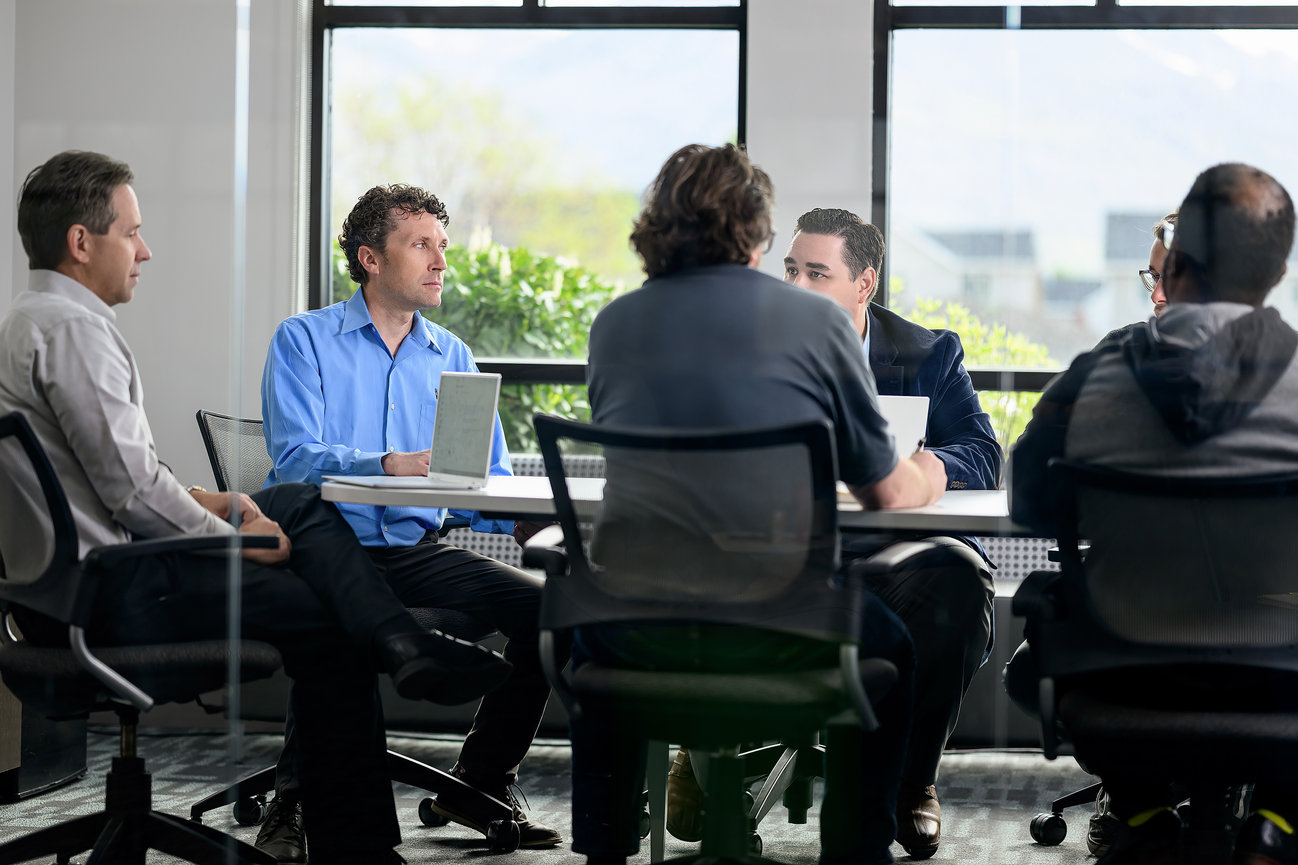 Group of six professionals engaged in a meeting around a conference table, discussing documents.