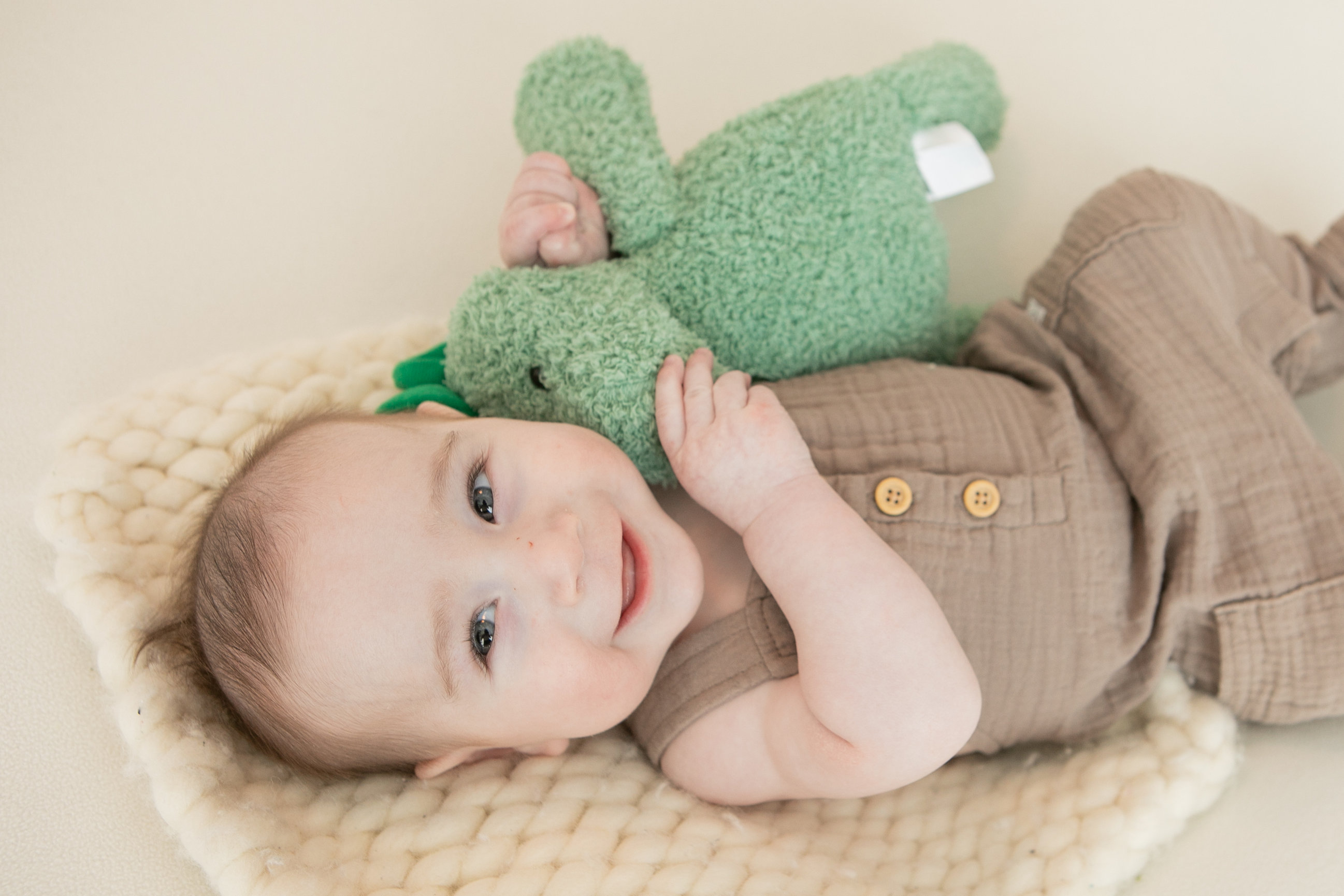 Baby holding a knitted green toy on a cream blanket