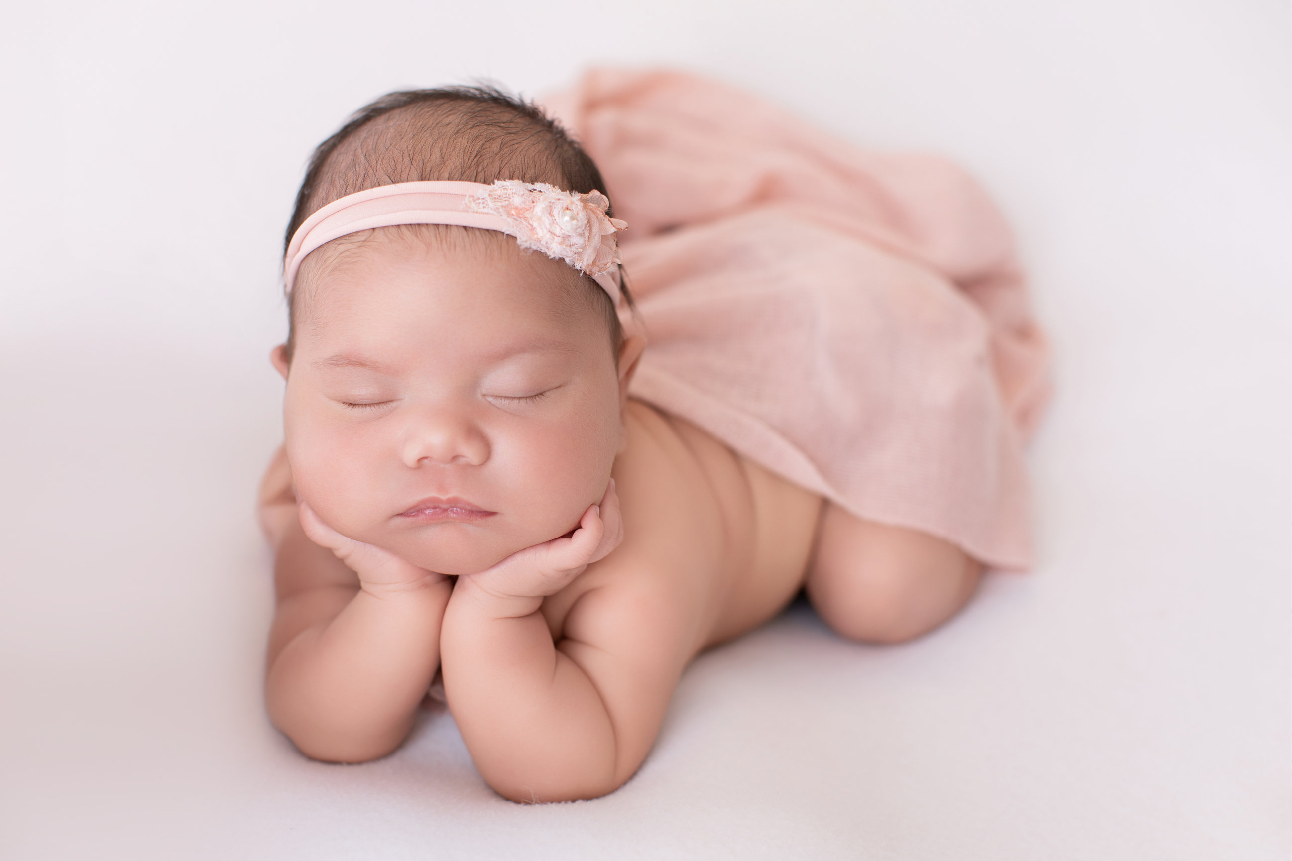 Sleeping newborn girl with her hands under her cheeks in a blush pink setup