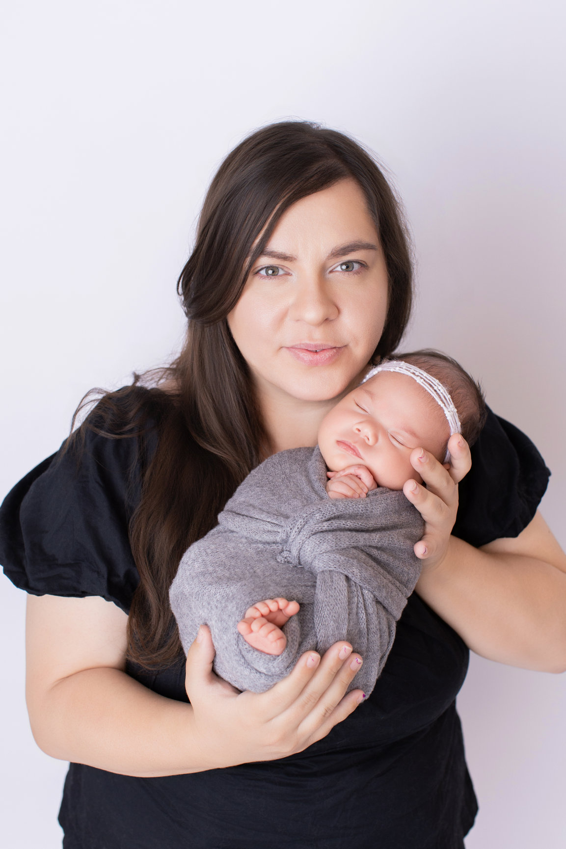 Mother cradling her newborn daughter wrapped in a soft grey wrap