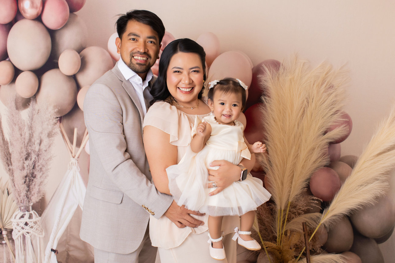 Parents holding their daughter together in a blush first birthday studio set