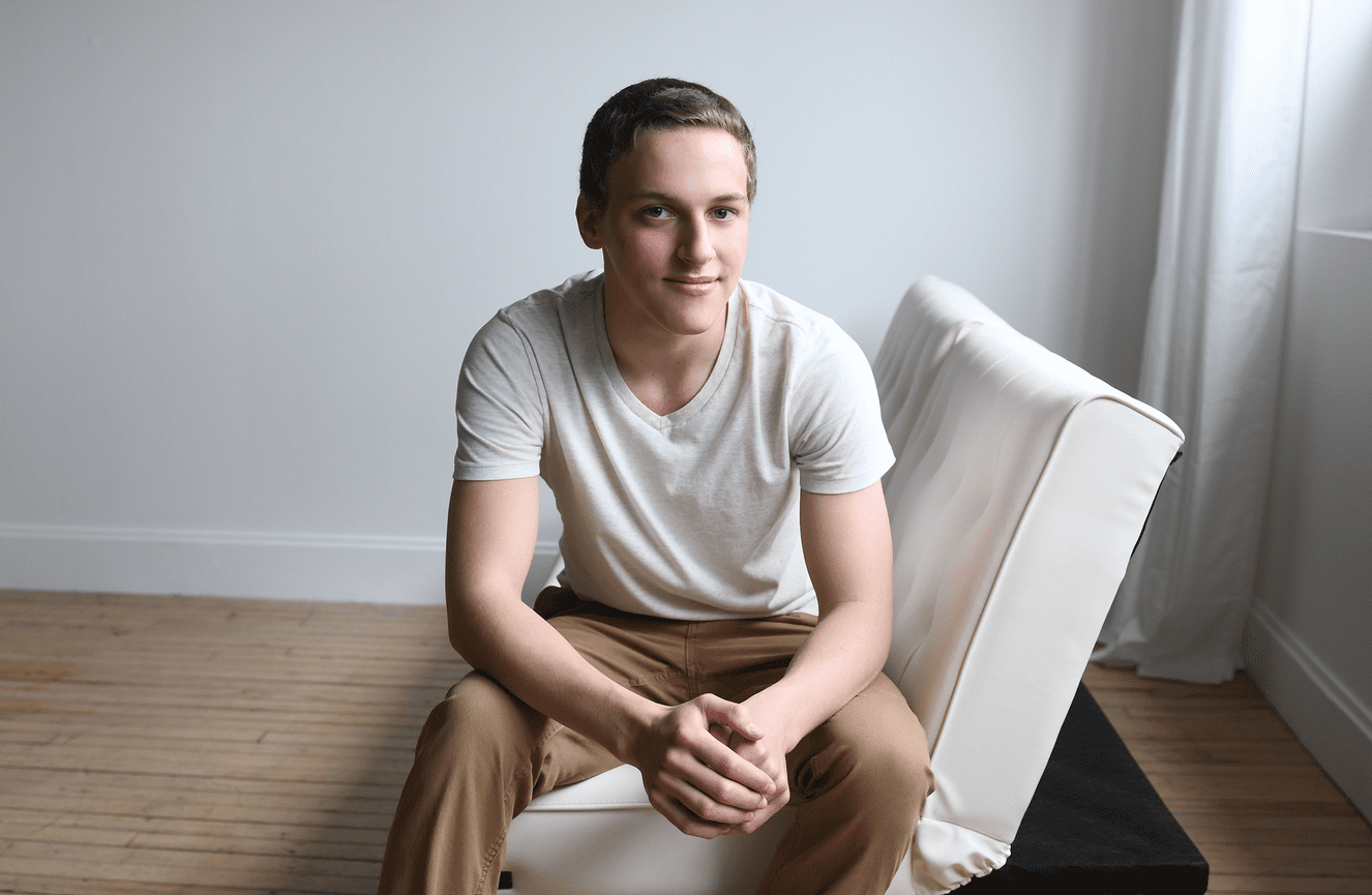 A young man in a classic white t-shirt sits on a couch.