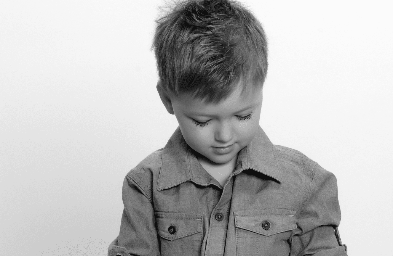 A young boy in a jean shirt shyly looking down during his children's photo session at Kliks Photography.