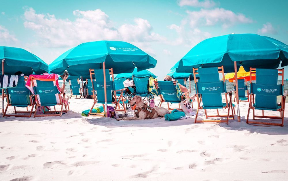 Turquoise beach chairs and umbrellas on a sandy beach under a partly cloudy sky.