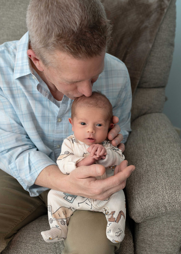 Father kissing newborn baby on the forehead while holding them on a couch