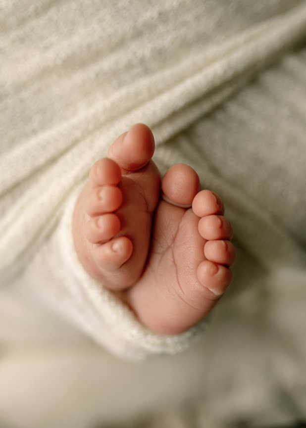 Tiny baby feet with soft, rounded toes, resting on a light fabric background.