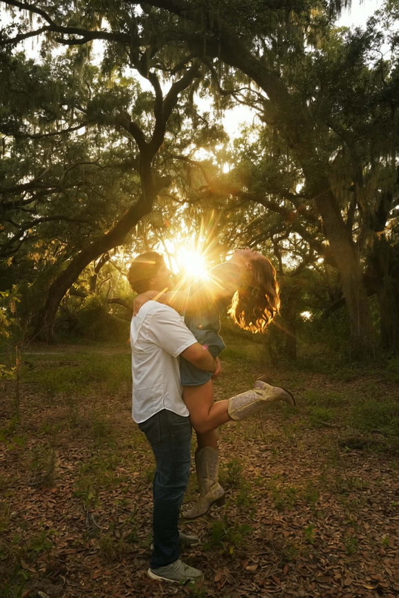 Couple embracing with sunlight glowing through the trees behind them.