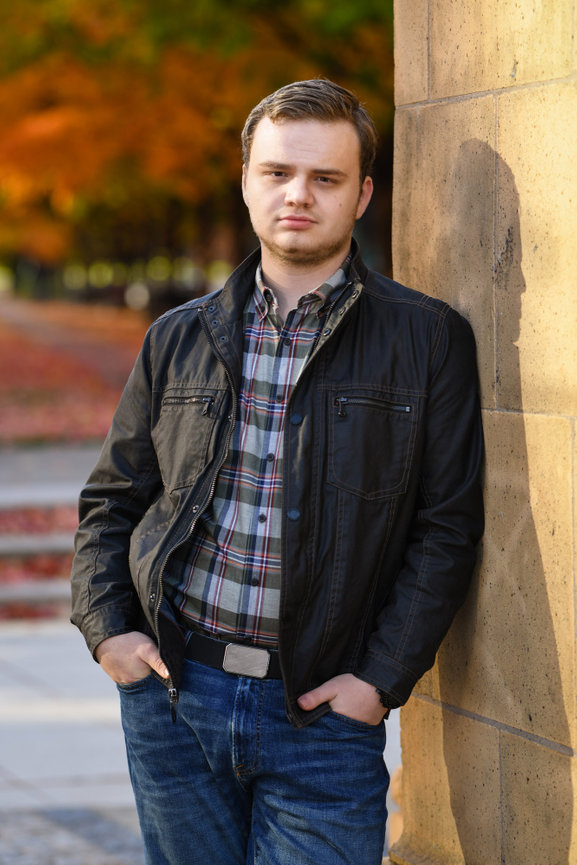 Teenage boy in a black jacket and jeans leaning against a wall in an urban setting for his senior pictures in Dublin OH.