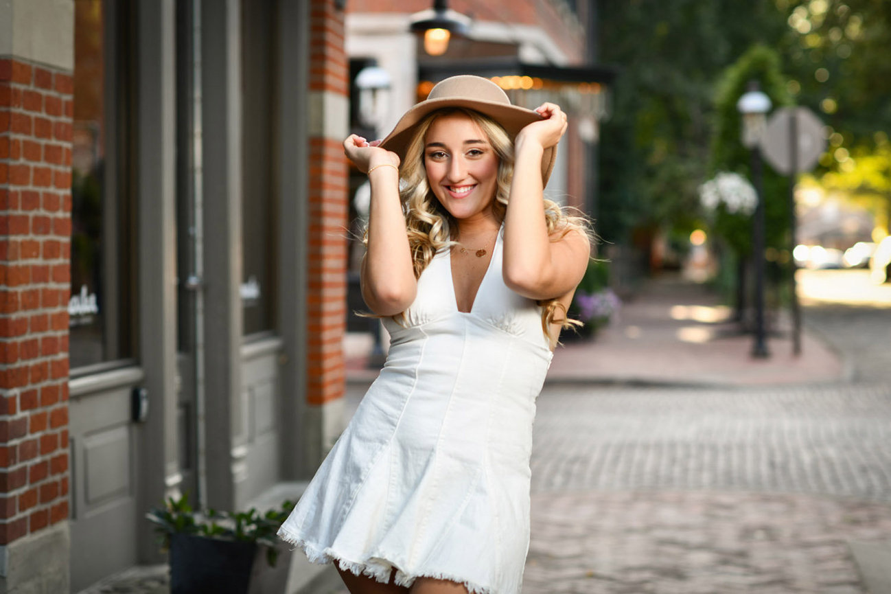 Blonde teenage girl in a white dress with a tan hat on an urban cobblestone street in Dublin OH.