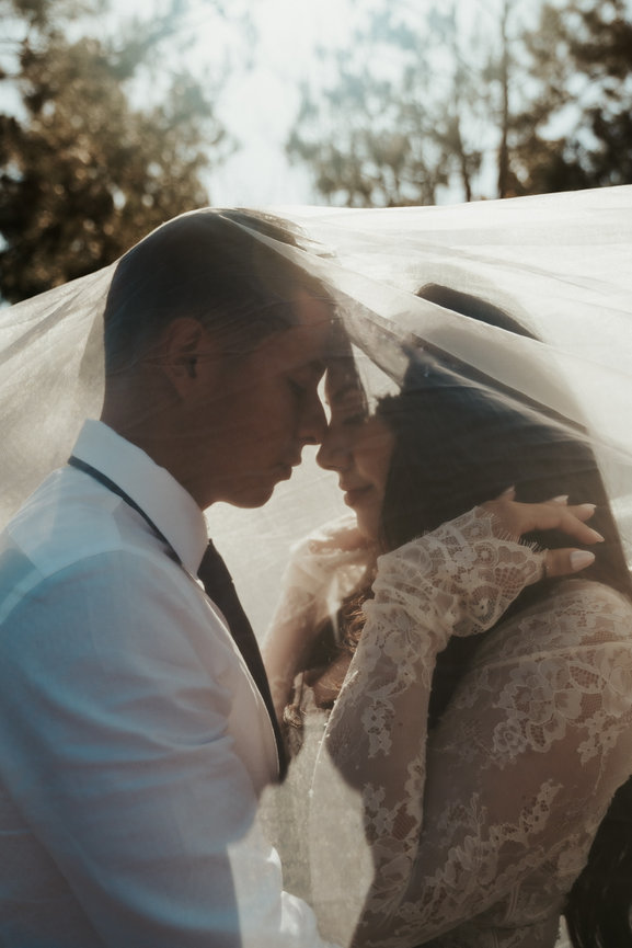 Couple touching foreheads under a veil outdoors