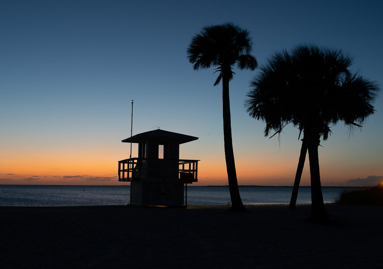 Dark blue and orange sunset frames the silhouette of the life guard station and palm trees at Fred Howard Park in Tampa Florida.